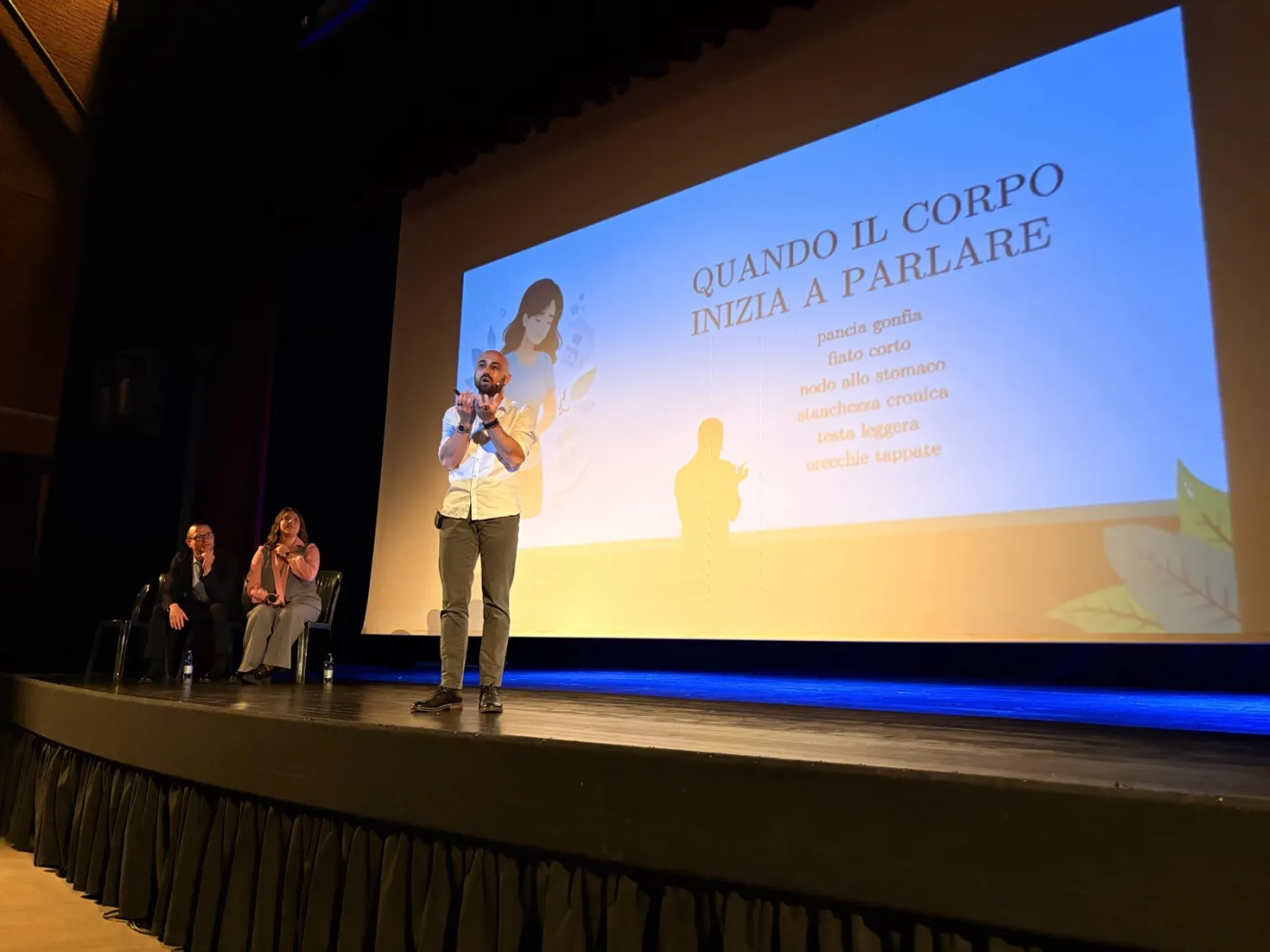 Francesco Sgarzi sul palco a teatro, davanti alla slide 'Quando il corpo inizia a parlare'